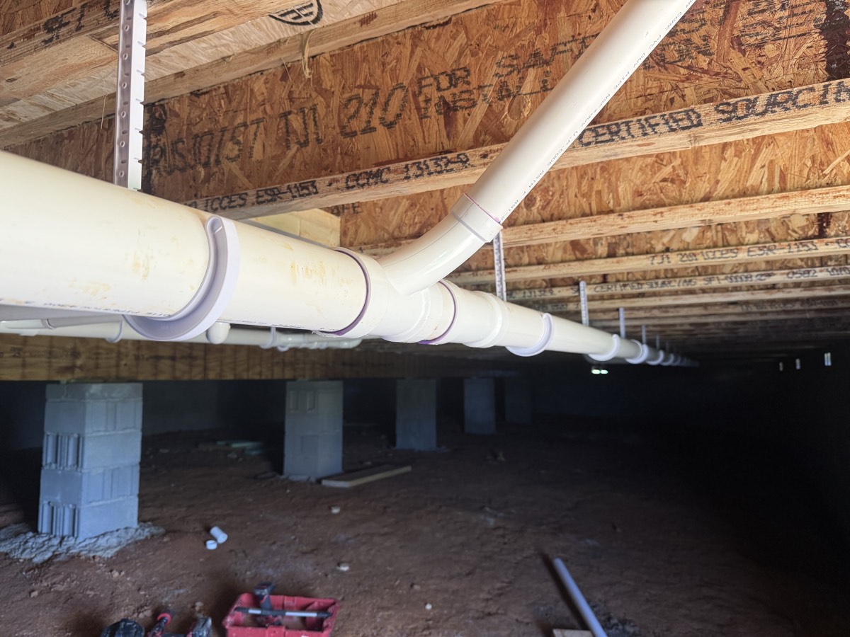 Newly installed PVC drain and waste lines running beneath a home